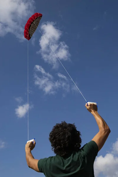 Giovane uomo che controlla un aquilone rosso nel cielo blu . — Foto Stock