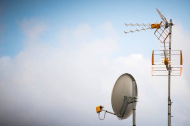 Mavi gökyüzü arkaplanlı televizyon antenleri ve parabolik çanaklar. Sol tarafında kopyalama alanı olan duvar kağıdı.