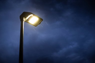 Alacakaranlıkta aydınlık sokak lambası. Huysuz mavi gökyüzü ve yağmur yağıyor. Sağ tarafta kopyalama alanı olan kasvetli ve ürkütücü arkaplan.