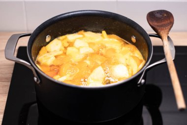 Ev yapımı kayısı reçeli, yanında tahta kaşıkla siyah bir tencereye tutturulmuş. Endüksiyon sobasında mevsimlik meyve korunumu hazırlanıyor.