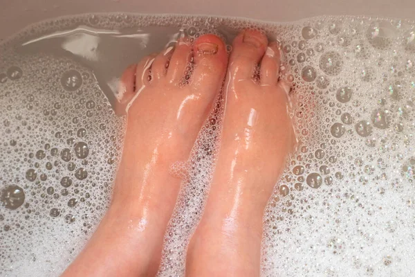 Washing little child feet in bubbling and foamy water. Close-up.