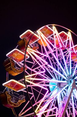 Geceleri renkli dönme dolap, neon ışıklarla aydınlatılıyor. Rosolina Mare lunaparkı, Veneto, İtalya. Dikey görüntüyü detaylandır.
