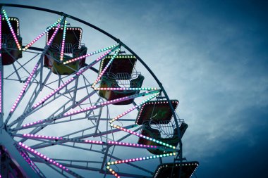 Alacakaranlıkta renkli dönme dolap, neon ışıklarla aydınlatılmış. Kopya alanı olan bir arkaplan. Tonlanmış, filtrelenmiş mavi renk. Rosolina Mare lunaparkı, Veneto, İtalya.