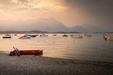 Pembe gün batımında Manerba del Garda, Garda Gölü, Lombardia, İtalya 'dan gelen tekneler ve kırmızı bir kanoyla göl manzarası.