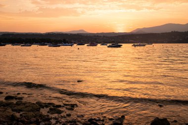 İtalya 'nın Manerba del Garda şehrinde günbatımında hala uzak teknelerle göl manzarası.