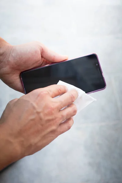 Erkek eller beyaz bir bezle akıllı telefon ekranını siliyor. Dikey çekim.