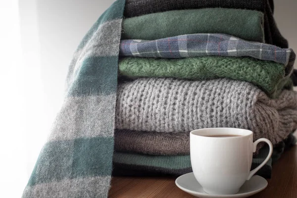 Yığınla yeşil ve gri süveter, yanında sıcak içecek beyaz bardak, arka planında fotokopi alanı, rahat, hygge ya da mevsimlik gardırop değiştiren duvar kağıdı..
