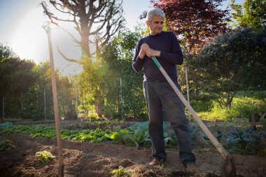 Elinde kürekle bahçesinde duran 70 yaşında bir adam. İşaret fişeği, ışık sızıntısı.