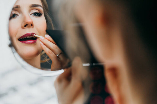 young  beautiful  bride applying lipstick  indoors