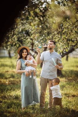 Parkta mutlu genç bir aile. Sabun kabarcıkları üfleme Adam 