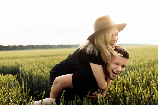 小麦畑の美しい若いカップル 女性にピギーバックライドを与える男 — ストック写真