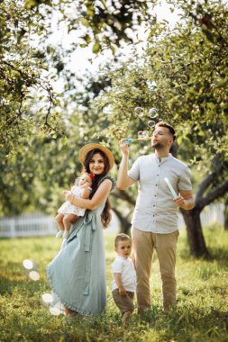 Parkta mutlu genç bir aile. Sabun kabarcıkları üfleme Adam 