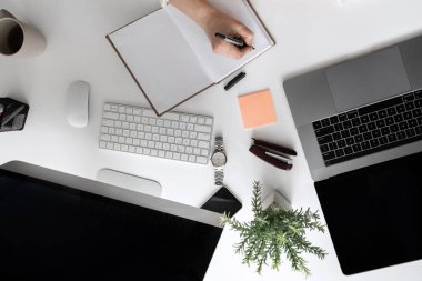 Not defterine, laptopuna, bilgisayarına yazı yazan bir kadın ile ofis masasının üst görünümü 