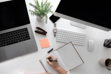 Not defterine, laptopuna, bilgisayarına yazı yazan bir kadın ile ofis masasının üst görünümü 