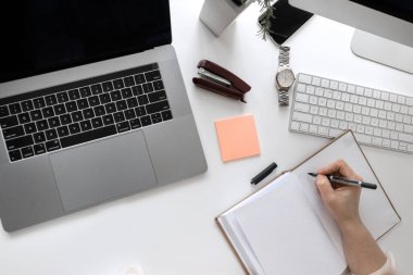 Not defterine, laptopuna, bilgisayarına yazı yazan bir kadın ile ofis masasının üst görünümü 