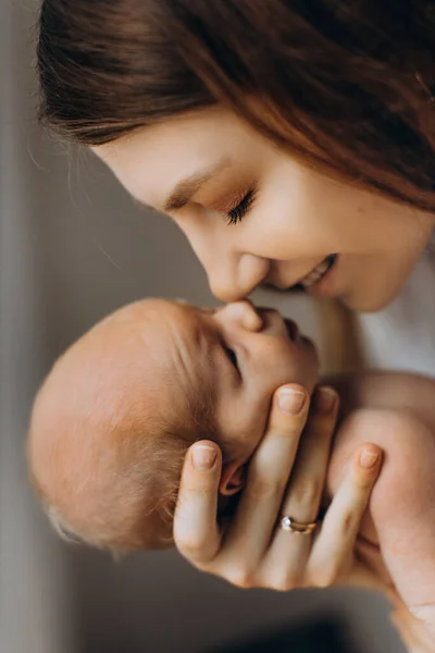 Mujer adorable sostiene a la niña recién nacida en brazos, madre cariñosa con hija pequeña toque suavemente con las narices, sonriendo, disfrute de momentos de crianza tierna, concepto de maternidad — Foto de Stock