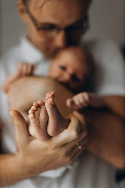 Handsome man hold newborn baby girl in arms, caring dad show to the camera tiny legs of little daughter, enjoy tender parenting moments, smiling, fatherhood concept — Stock Photo, Image