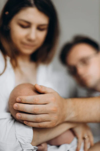 Hermosa familia con niña recién nacida, madre encantadora sostiene a la pequeña hija en brazos, padre cariñoso toca suavemente a la adorable niña, momentos familiares felices, concepto de crianza — Foto de Stock