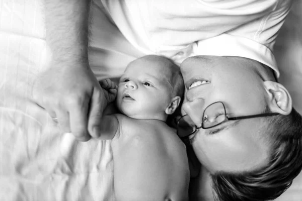 Milující otec s rozkošné novorozeně holčička ležící v posteli, starostlivý táta držet malou ruku malé dcery, usmívající se, něžné rodičovské momenty, otcovství koncept — Stock fotografie