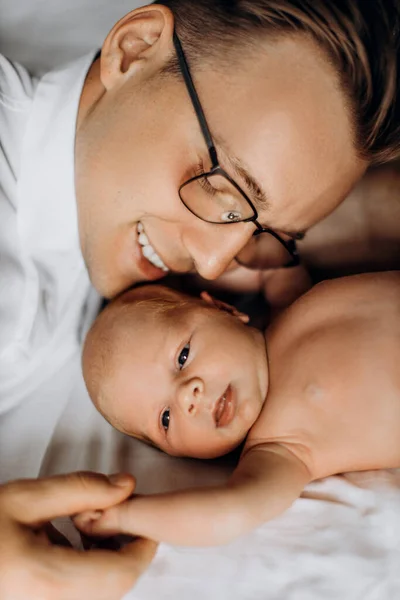 Портрет прекрасной новорожденной девочки, лежащей на кровати, заботливый папа держит крошечную руку маленькой дочери, нежные моменты воспитания, улыбаясь, отцовство концепции — стоковое фото