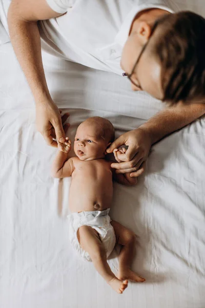 Portrait of lovely newborn baby girl laying at the bed, caring dad hold tiny arms of little daughter, tender parenting moments, smiling, fatherhood concept — Stock Photo, Image