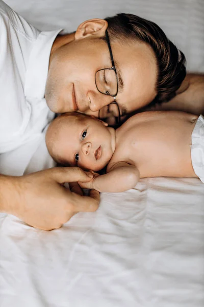 Любящий отец с очаровательной новорожденной девочкой лежа на кровати, заботливый папа держать крошечную руку маленькой дочери, улыбаясь, нежные моменты воспитания, отцовство концепции — стоковое фото