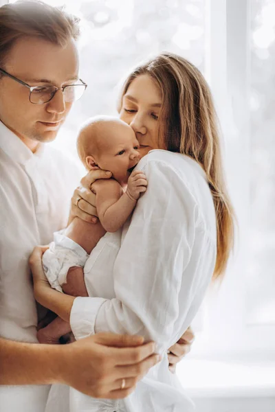 Beautiful parents with newborn baby girl, loving mom hold little daughter in arms, caring husband gently hug adorable wife, smiling, enjoy tender family moments, parenting concept — Stock Photo, Image