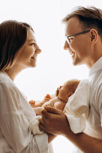 Счастливая молодая семья с маленькой дочкой, красивая мать держит милого новорожденного на руках, заботливый отец держит за руки восхитительную девочку, мама и папа улыбаются, прощаясь с понятием — стоковое фото
