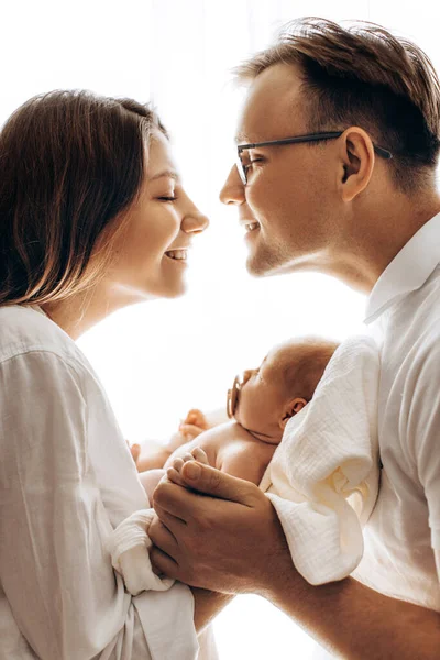 Feliz familia joven con hija pequeña, hermosa madre sostiene lindo bebé recién nacido en brazos, padre cariñoso toma de la mano de la niña adorable, mamá y papá sonriendo, concepto de crianza — Foto de Stock