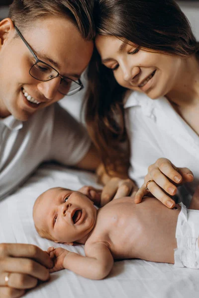 Cute newborn baby laying at the bed with caring parents, loving dad gently hold arms of little daughter, happy mom smiling, young family spend time together, parenting concept — Stock Photo, Image