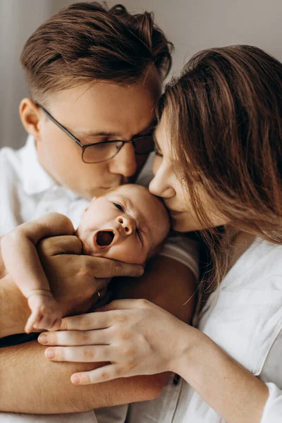 Gelukkige ouders met schattige pasgeboren baby meisje, knappe vader houden kleine dochter in de armen, mooie vrouw en liefhebbende man zachtjes kus hun kind, jong familie concept — Stockfoto