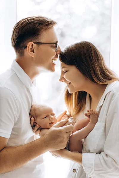 Счастливая молодая семья с маленькой дочкой, красивая мать держит милого новорожденного на руках, заботливый отец держит за руки восхитительную девочку, мама и папа улыбаются, прощаясь с понятием — стоковое фото