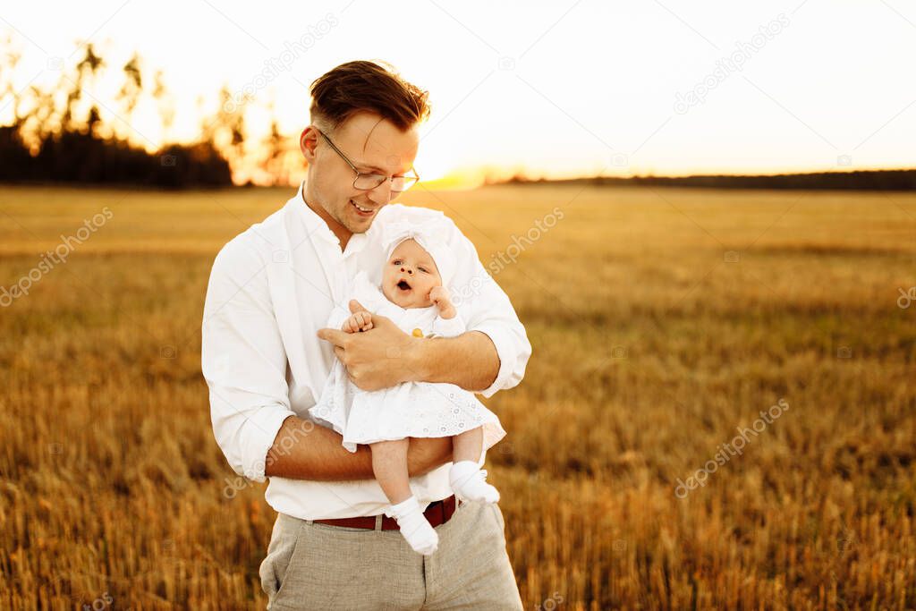 Handsome father with adorable little daughter at the field, caring dad hold cute newborn baby girl in arms, tender family moments, parenting and fatherhood concept 