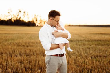 Tarlada sevimli bir kızı olan yakışıklı bir baba, şefkatli bir baba yeni doğmuş bebeği kollarına alıyor, tatlı çocuğu, ebeveynliği ve babalık kavramını nazikçe öpüyor.