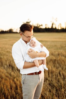 Tarlada sevimli bir kızı olan yakışıklı bir baba, şefkatli bir baba yeni doğmuş tatlı bir bebeği kollarına alıyor, hassas aile anları, ebeveynlik ve babalık kavramları. 