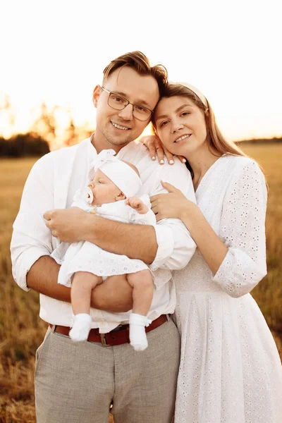 Retrato de una hermosa familia con una hija pequeña, un padre guapo sostiene a una linda niña recién nacida en brazos, una hermosa madre sonriendo, paternidad y concepto de infancia — Foto de Stock