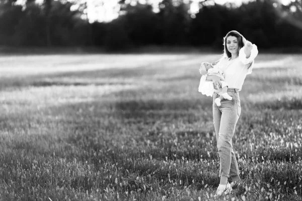 Hübsche Frau mit süßem neugeborenen Mädchen, das auf dem Feld geht, liebevolle Mutter hält schöne kleine Tochter in den Armen, genießt glückliche Momente mit Kind, Umstandskonzept — Stockfoto