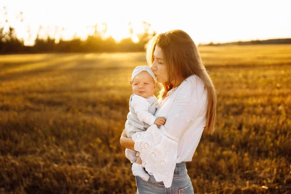 Adorável mãe com bela filhinha no campo, mulher bonita segurar bebê recém-nascido bonito nos braços, mãe carinhosa beijar suavemente pequena menina bebê, conceito de maternidade — Fotografia de Stock