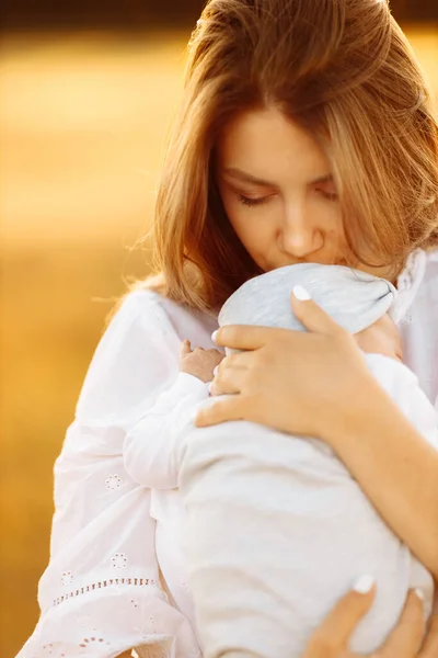 Imádnivaló anya gyönyörű kislánya a pályán, csinos nő tart aranyos újszülött baba karjaiban, gondoskodó anya gyengéden megcsókolja apró baba lány, anyaság koncepció — Stock Fotó