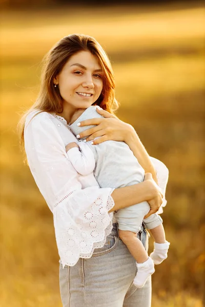 Спокойная женщина с красивой новорожденной девочкой на поле, счастливая мама держит симпатичную маленькую дочку на руках, улыбается, наслаждается каждым моментом прощания, материнства — стоковое фото