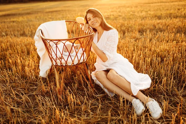Adorable woman sitting near tiny bed with lovely newborn baby girl at the field, caring mother enjoy tender moments with little daughter, parenthood and motherhood concept
