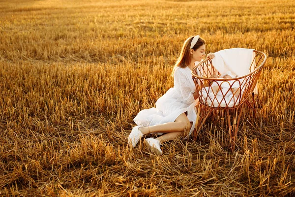 Elegant woman near the tiny bed with beautiful newborn baby girl at the field, loving mother take care of little daughter, tender family moments, parenting and maternity concept