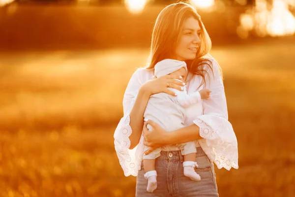 Hübsche Frau mit netten neugeborenen Mädchen auf dem Feld, liebevolle Mutter hält schöne kleine Tochter in den Armen, genießen glückliche Momente mit Kind, Umstandskonzept — Stockfoto