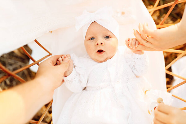 Portrait of newborn baby girl laying in the bed, happy parents hold tiny hands of little daughter, cute child look around with big interest, parenthood and childhood concept  