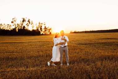 Mutlu ebeveynler ve yeni doğmuş güzel bir kız bebek, tarlada yürüyor, şefkatli baba kucağında küçük kız, güzel anne yakışıklı babaya sarılıyor, gülümsüyor, genç aile kavramı