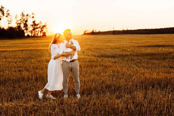 Happy parents with lovely newborn baby girl walking at the field, caring dad hold in arms little daughter, beautiful mother hugging handsome father, smiling, young family concept — Stock Photo, Image