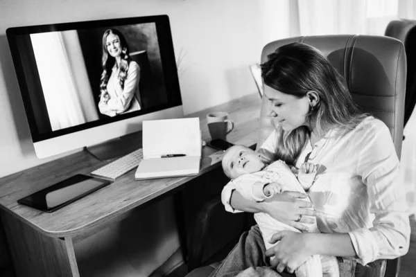 Boldog fiatal anya ül az asztalnál, tartsa a karját kislánya, gyönyörű hölgy szünetet a baba lány, mosolygós, üzletasszony dolgozik az otthoni online — Stock Fotó
