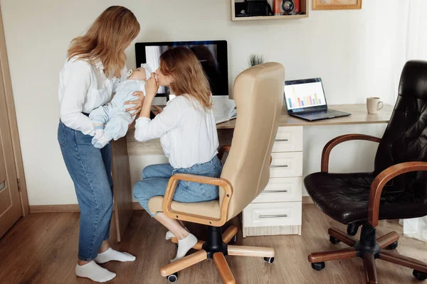 Jeune mère s'asseoir à la chaise, prendre une pause pour passer du temps avec la petite fille, dame d'affaires travaillant à la maison en ligne, tout en s'occupant grand-mère baby-sitting avec la petite fille nouveau-née — Photo