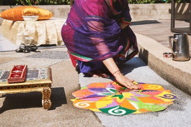 Women decorating and coloring tradition colorful rice art or sand art (Rangoli) on the floor with paper pattern using dry rice and dry flour with colored from natural pigments like sindoor, haldi (turmeric) clipart