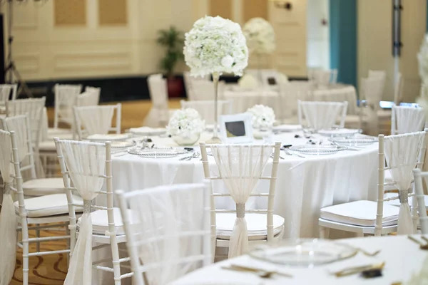 The wedding reception dinner venue setup with the white flower theme, A bunch of white roses, flower, floral decoration on the dinner table.